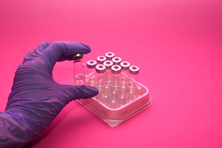 ampoules in a box on a pink background. a hand in a blue medical glove takes ampoules. human and...