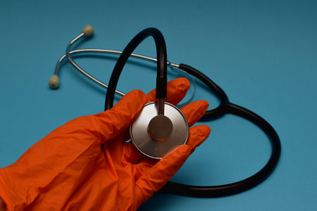 hand in an orange medical glove holds a stethoscope against blue background. human and veterinarian medicine conceptの写真素材
