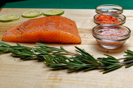 salmon fillet, pink salt, rosemary and dried carrots in glass bowls on a wooden boardの写真素材