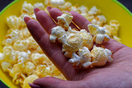 Yellow bowl full with popcorn close-up. Lots of popcorn in women hand. Film preparation conceptの写真素材