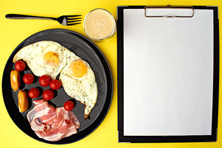 A healthy breakfast - coffee, scrambled eggs, bacon, cheese and cherry tomatoes. Food in a black...
