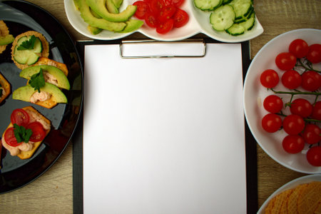 Notepad with a white sheet of paper for notes. Around a snack of crackers and chopped vegetables. To-do list. Copy space.の写真素材