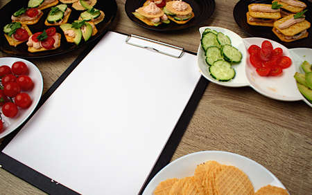 Notepad with a white sheet of paper for notes. Around a snack of crackers and chopped vegetables. To-do list. Copy space.の写真素材