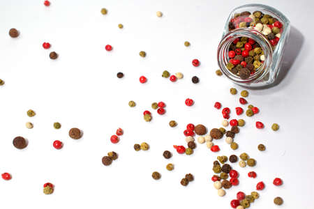 A glass jar with a mixture of five peppers. Multi-colored seasoning grains. Grains are scattered...