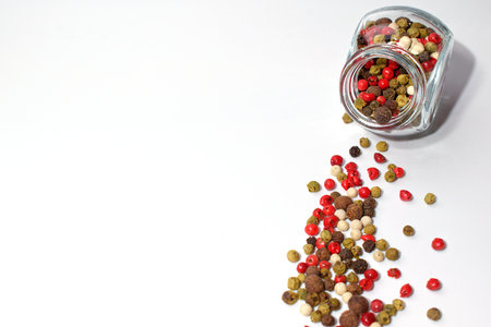 A glass jar with a mixture of five peppers. Multi-colored seasoning grains. Grains are scattered nearby. Isolate.の写真素材