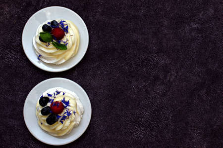 Dessert Madame Pavlova with fresh raspberries and blueberries, decorated with mint and cornflower flowers. Light dessert with meringue and cream. Copy space. Flat lay.の写真素材