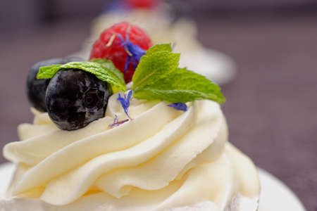 Dessert Madame Pavlova with fresh raspberries and blueberries, decorated with mint and cornflower flowers. Light dessert with meringue and cream.の写真素材