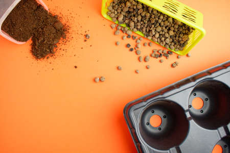 Expanded clay in a green basket, plastic pot and ground on an orange background. Plant transplant concept. Copy space. Flat lay.の写真素材