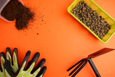 Expanded clay in a green basket, green fertilizer, ground and hoe on an orange background. Plant transplant concept. Copy space.の写真素材