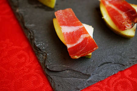 A slice of jamon on a pear, a traditional holiday snack. A snack on a stone board on a table with a...