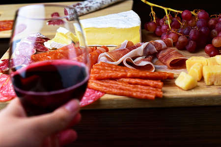 In focus on a wooden board, sliced lard and fuet, cabanos sticks, grapes, brie cheese, diced...