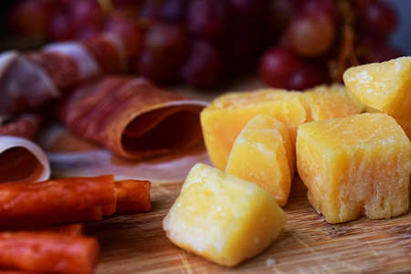 Close-up of hard cheese cubes, shallow depth of field. Parmesan on wooden board. Wine appetizer.