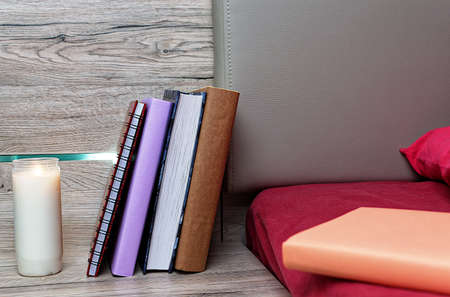 There are books, candle and a notebook near the bed with a pillow.