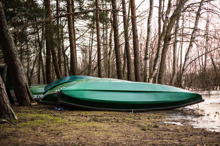 Several green upturned fishing boats lie on the shore near a lake in a mixed forest in Latvia.の写真素材