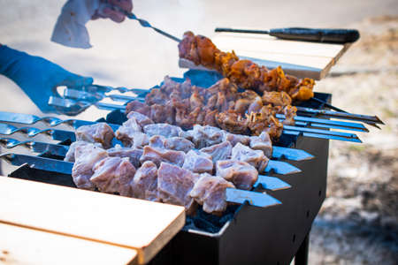 In the frame, delicious, juicy, chicken and pork kebabs on skewers are grilled on the grill. On a sunny day, outdoor recreation with barbecue. Smoke rises from the barbecue above the barbecue.の写真素材