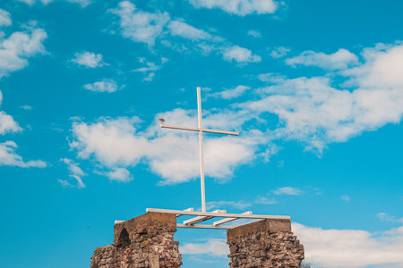 A white wooden cross against a blue sky with clouds, a seagull sits on the edge.の写真素材