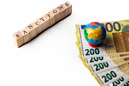 Isolate of wooden letters folded into the word sanctions, money and small globe nearby.