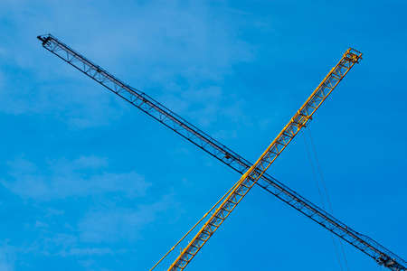Construction cranes are crossed in the sky against the blue sky.