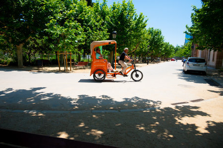 Spain, Barcelona - May 30 2022: Cyclo rickshaw of orange color with tourists rides in the Ciutadella Park in Barcelona, Spain.のeditorial素材