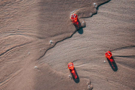 Three red dice lie on the sand on the shore and the water washes them. copyspace.の写真素材