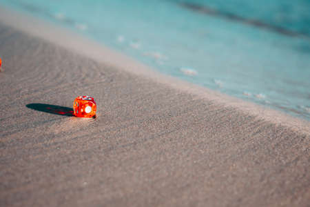 One red dice lie on the sand on the shore and the water washes them. copyspace.の写真素材