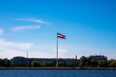 Latvian Flag Hang On Flagpole Against Blue Sky, On Banks Of Daugava River.の写真素材