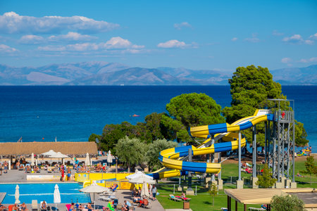 Moraitika, Greece - 09 22 2022: View on Ionian Sea and Greece Balkan Peninsula, People Sunbathe And Relax Beside Pool With Waterslides in Hotelのeditorial素材