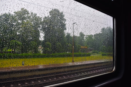 View from the train window on rainy weather in summer. The train window is covered in raindrops.