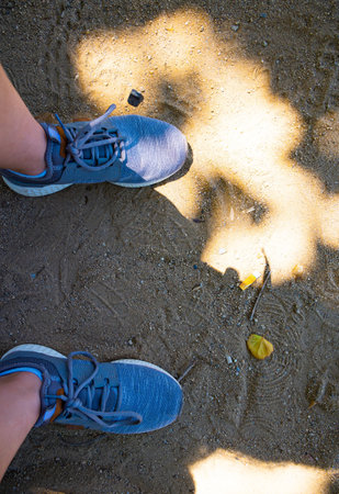 Top Down View Of Womans Legs In Gray Sneakers On Country Road. Concept Of Comfortable Shoes For Long...