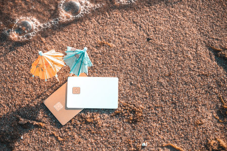 Top View Of Wet Sand With Bank Cards And Cocktail Umbrellas. Concept Of Limitless Possibilities. Concept Of Reliability Of Bank Cards With Completed Transactions and Expenses Tracking On Beach Holiday.の写真素材