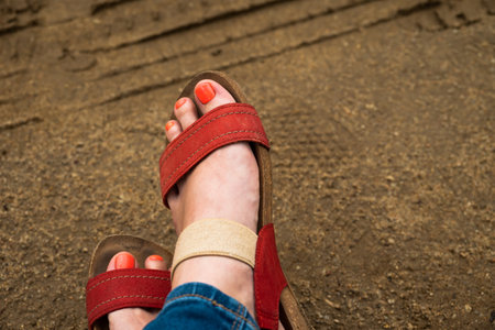 Womens legs in red sandals on a sandy road. The concept of walking and the opportunity to stop and rest.の写真素材