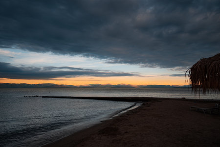 Romantic landscape - Sunrise, soft orange sky, illuminated mountains, sea, beach, pier and beach lounger with an umbrella. The concept of a date and a meeting of the sunrise at the sea.の写真素材