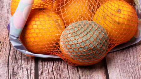 In a mesh bag with oranges there is one spoiled orange with mold.の写真素材