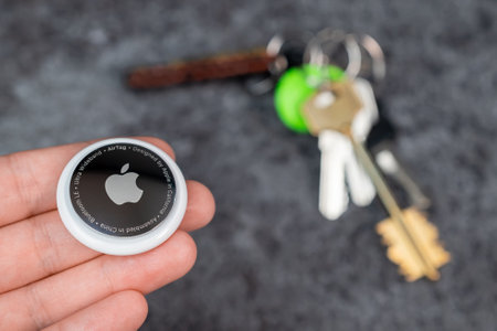 Jurmala, Latvia - 21 09 2023: Woman holds AirTag in her hands, and the keys to the apartment are out of focus in the background. Air Tag help track keys.のeditorial素材
