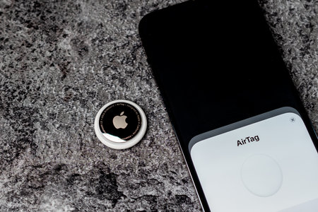 Jurmala, Latvia - 21 09 2023: AirTag Apple lies on table nex to smartphone witch are connected to tag. Air Tag gadget to track of your stuff.のeditorial素材