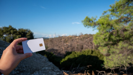 In a woman's hand, a white card against a background of a burned forest on the island of Rhodes. The...