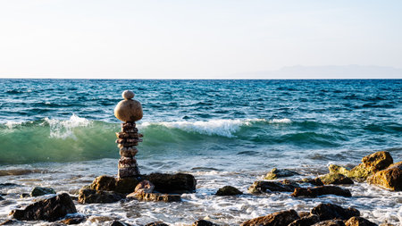 A rock formation is standing on a rocky beach next to the ocean. The rocks are scattered around the formation, and the waves are crashing against the shore. The scene is peaceful and sereneの写真素材