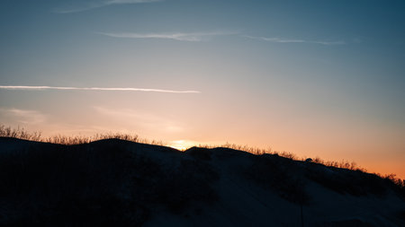 A beautiful sunset over a hillside with a small hill in the foregroundの写真素材