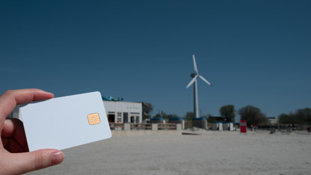 A person holding a credit card in front of a wind turbine