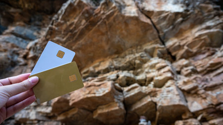 In front of a rocky wall, a person is holding two credit cardsの写真素材