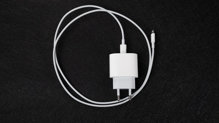 Jurmala, Latvia 25.06.2024: A white Apple lightning charger on black surface with electronics...