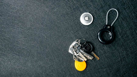 Jurmala, Latvia - 25 06 2024: A group of keys and a keychain placed on a darkcolored flat surface with Apple Airtag.のeditorial素材