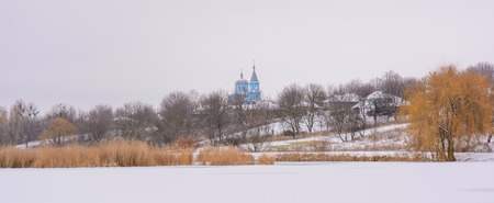 Photo of Church in the village behind the lake covered with snowの写真素材