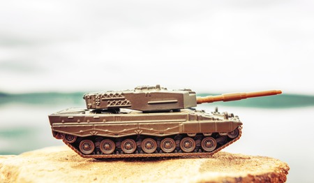 Toy tank on beautiful nature background with blue sky and lakeの写真素材