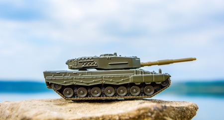 Toy tank on beautiful nature background with blue sky and lake