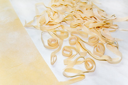 Closeup cooking italian pasta. Flat-lay with flour, dough and sliced fettuccine. Use as a culinary background, a recipe book.の写真素材