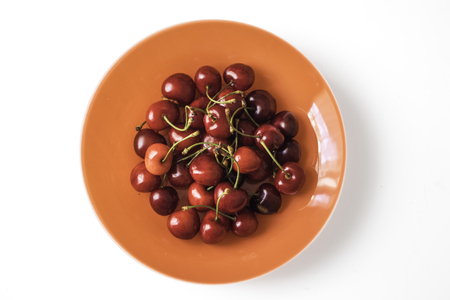 Orange plate full of sweet red cherries on a white backgroundの写真素材