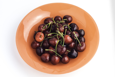 Orange plate full of sweet red cherries on a white backgroundの写真素材