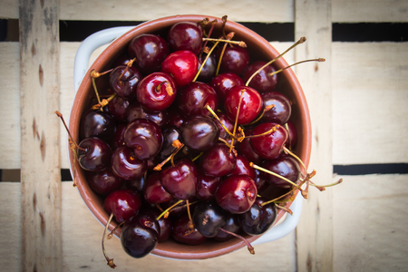 Terracotta bowl full of cherries on a rough wooden backgroundの写真素材