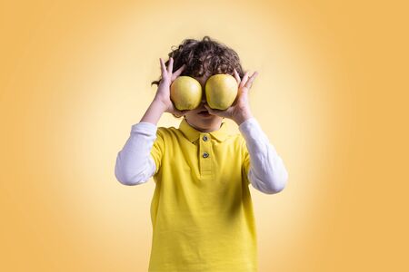 Kid hiding his eyes with two apples. Fruit and healthy fruit diet for children conceptの写真素材